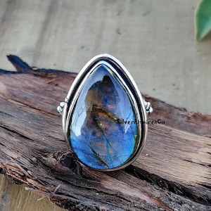 Könnte beinhalten: Ein silberner Ring mit einem tropfenförmigen blauen Labradorit-Edelstein. Der Ring hat ein schlichtes, elegantes Design und ist in eine silberne Fassung gefasst.