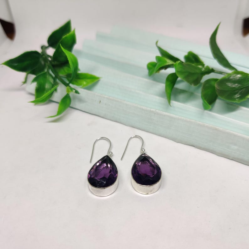 May include: A pair of silver dangle earrings with teardrop-shaped purple amethyst stones.