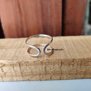 Könnte beinhalten: Ein silberner Ring mit einem einzigartigen offenen Design. Der Ring besteht aus einem einzigen Stück Metall, das zu einer Schleife mit einer Lücke in der Mitte gebogen ist. Der Ring ist schlicht und elegant und wäre ein tolles Geschenk für einen besonderen Menschen.