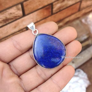 May include: A teardrop-shaped pendant made of silver with a large, deep blue lapis lazuli stone.