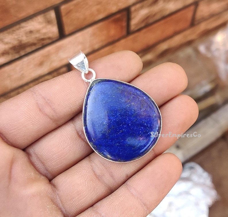 May include: A teardrop-shaped pendant made of silver with a large, deep blue lapis lazuli stone.