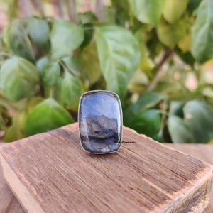 Könnte beinhalten: Ein silberner Ring mit einem großen, rechteckigen, dunkelblauen Labradorit-Edelstein. Der Ring liegt auf einer Holzoberfläche.