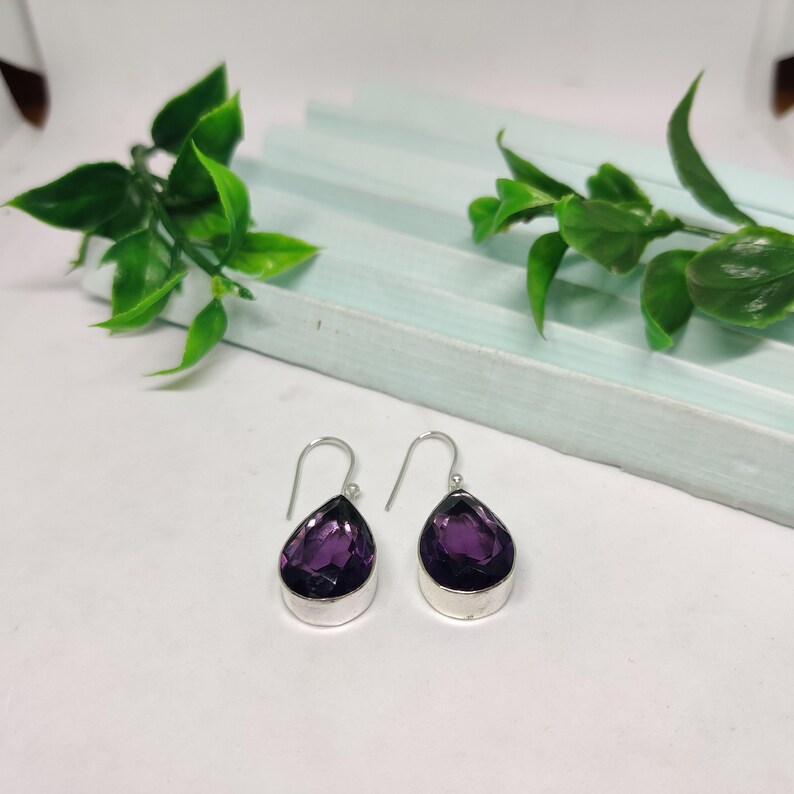 May include: A pair of silver dangle earrings with teardrop-shaped purple amethyst stones.
