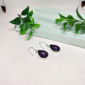 May include: A pair of silver dangle earrings with teardrop-shaped purple gemstones.