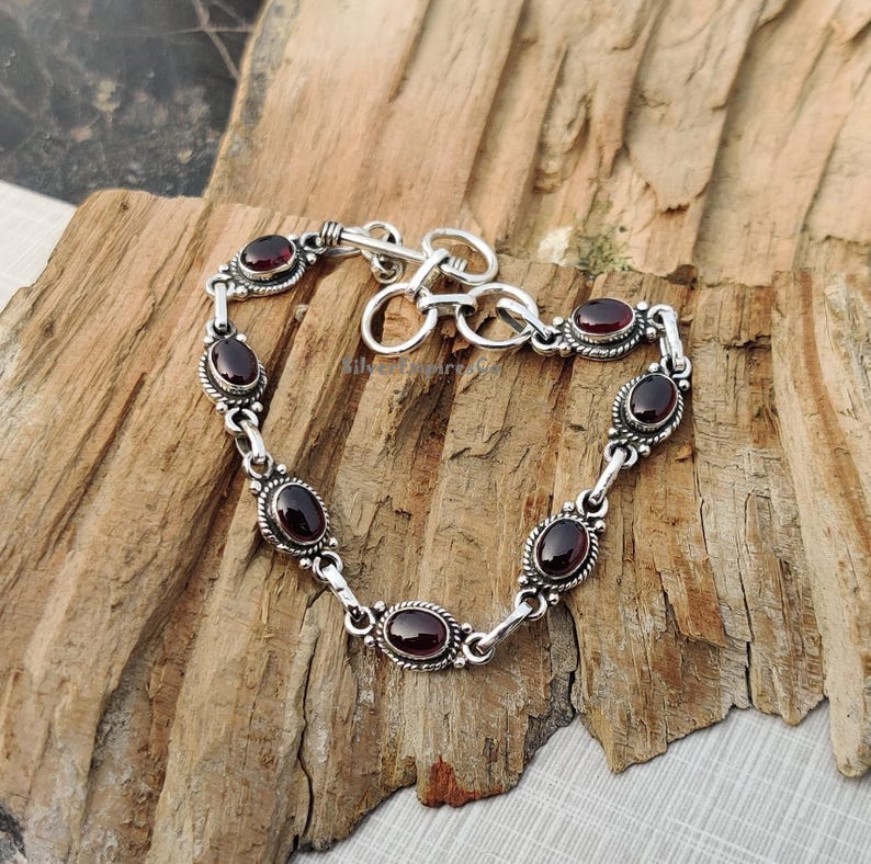 May include: A silver bracelet with a toggle clasp and six oval-shaped red gemstones.