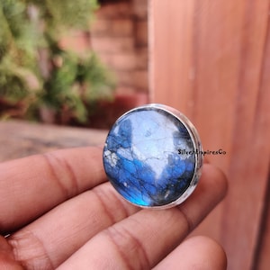 May include: A silver ring with a large, round, blue labradorite gemstone. The stone has a shimmering, iridescent effect.