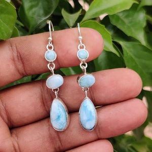 Könnte beinhalten: Ein Paar silberne Ohrhänger mit blauen und weißen Edelstein-Tropfen. Die Ohrringe haben eine Tropfenform und sind mit kleineren runden Edelsteinen verziert.
