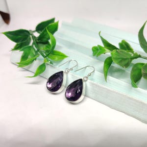 May include: A pair of silver dangle earrings with teardrop-shaped amethyst gemstones.