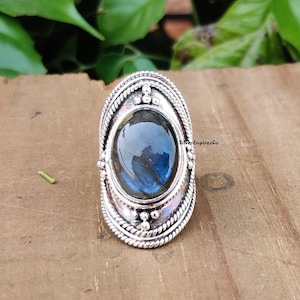 May include: A silver ring with a large oval blue labradorite gemstone set in a detailed silver bezel. The ring has a rope-like design around the band.