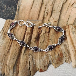 May include: A silver bracelet with a toggle clasp and oval-shaped red gemstones.
