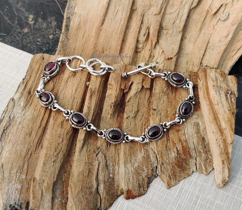 May include: A silver bracelet with a toggle clasp and oval-shaped red gemstones.