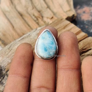 Puede incluir: Un anillo en forma de lágrima con una piedra preciosa azul y blanca engastada en una banda de plata.