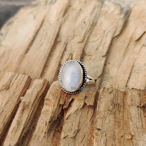 May include: A silver ring featuring a white oval moonstone set in a twisted rope design band.