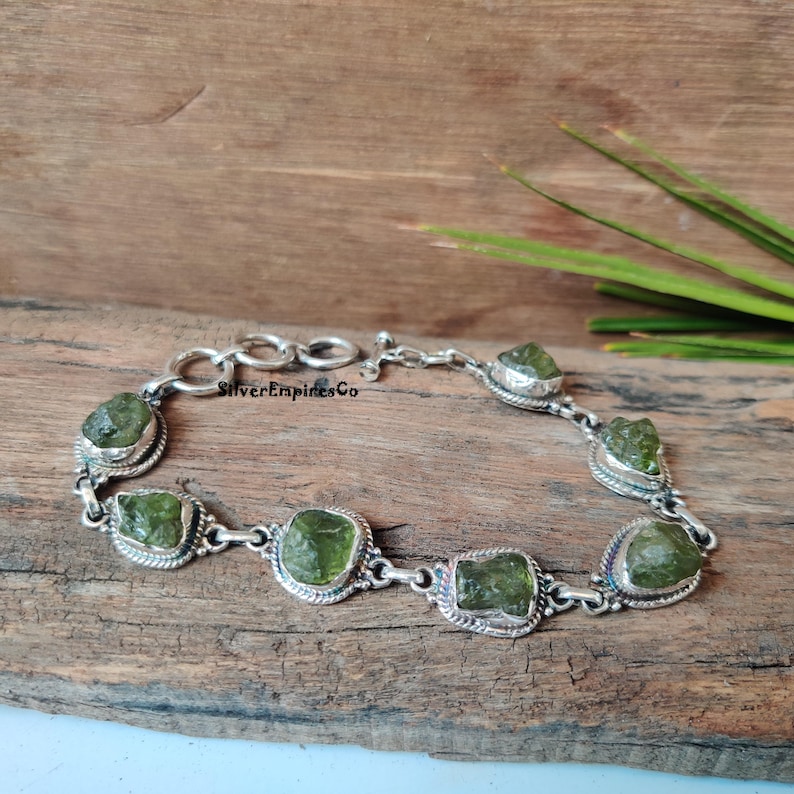 May include: A silver bracelet with a chain link design and seven green gemstone accents. The gemstones are rough and irregular in shape, giving the bracelet a rustic look.