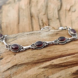 May include: A silver bracelet featuring five oval-shaped red gemstones. The bracelet has a delicate chain design.