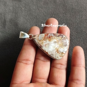 May include: A teardrop-shaped pendant with a silver bail and a brown, white and red agate stone. The stone has a swirling pattern and a white centre.