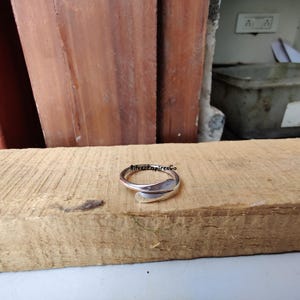 Könnte beinhalten: Ein silberner Ring mit einem einzigartigen, geschwungenen Design. Der Ring ist offen und verstellbar, um verschiedenen Fingergrößen zu passen.