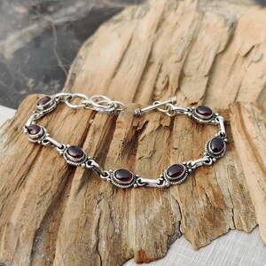 May include: A silver bracelet with a toggle clasp and six oval-shaped red gemstones.
