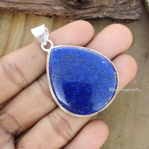 May include: A silver pendant featuring a large, teardrop-shaped lapis lazuli stone. The stone is a deep blue colour with flecks of gold.
