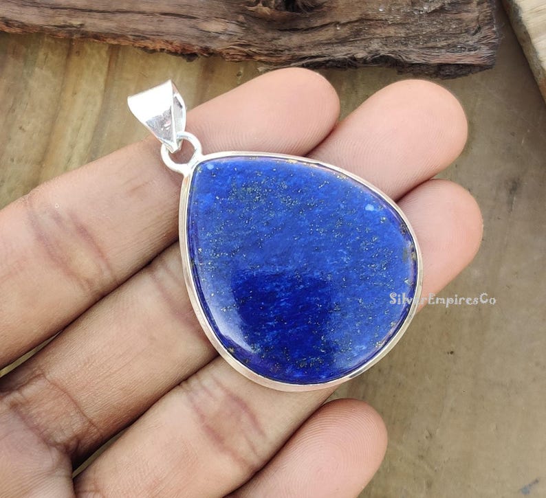May include: A silver pendant featuring a large, teardrop-shaped lapis lazuli stone. The stone is a deep blue colour with flecks of gold.
