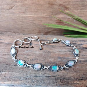 Op de afbeelding: Een zilveren armband met een schuifgesp en ovale opaalstenen. De armband ligt op een houten oppervlak.