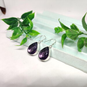 May include: A pair of silver dangle earrings with teardrop-shaped amethyst gemstones.