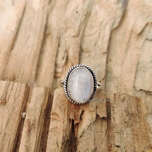 May include: A silver ring featuring a white oval moonstone set in a rope-like design.