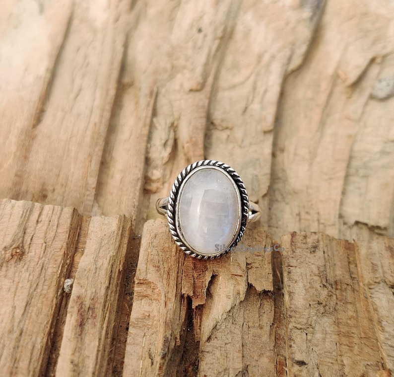 May include: A silver ring featuring a white oval moonstone set in a rope-like design.