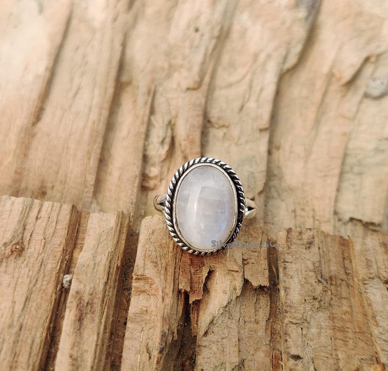 May include: A silver ring featuring a white oval moonstone set in a rope-like design.