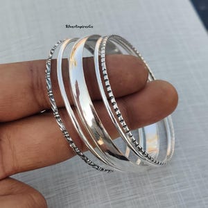 Pode incluir: Conjunto de quatro pulseiras de prata com diferentes designs texturizados. As pulseiras estão empilhadas umas sobre as outras.
