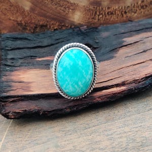 May include: A silver ring with a light blue oval-shaped gemstone set in a rope-like border.