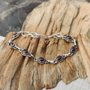 May include: A silver bracelet with a toggle clasp and six oval-shaped red gemstones.