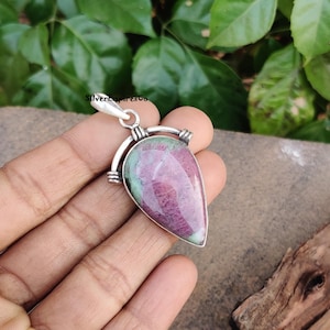 Könnte beinhalten: Ein silberner Anhänger mit einem rosafarbenen und grünen Edelstein. Der Anhänger hat die Form einer Träne und einen silbernen Öse.