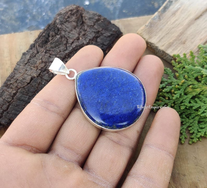 May include: A silver pendant featuring a large, teardrop-shaped lapis lazuli gemstone. The gemstone is a deep blue colour with flecks of gold.