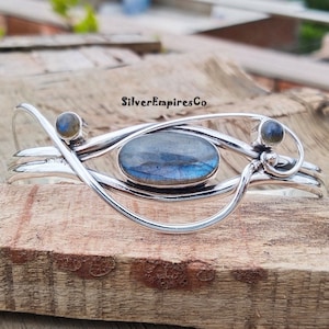 May include: Silver bracelet with a large oval labradorite gemstone and two smaller labradorite gemstones. The bracelet is made of silver wire and has a delicate, flowing design.