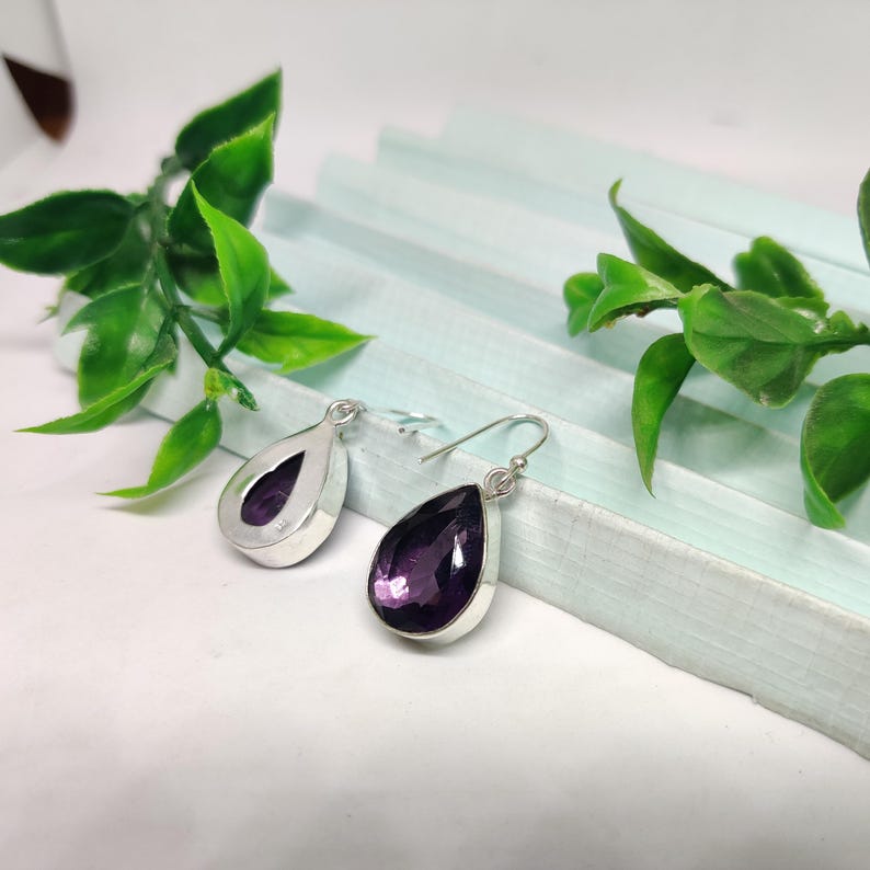May include: A pair of silver dangle earrings with teardrop-shaped amethyst gemstones.