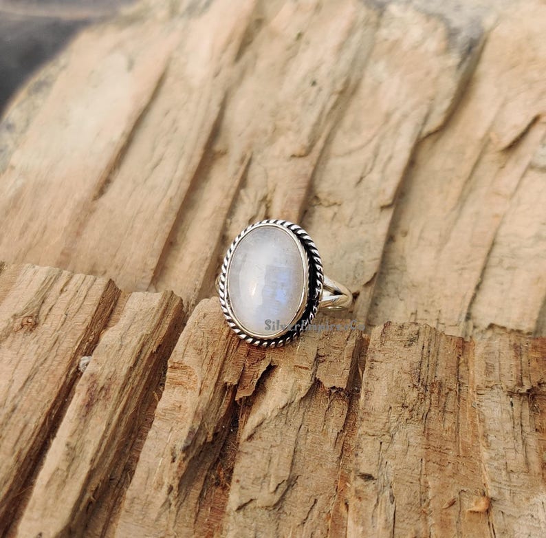 May include: A silver ring featuring a white oval moonstone set in a twisted rope design.