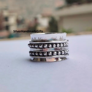 Könnte beinhalten: Ein silberner Fidget-Spinner-Ring mit mehreren strukturierten Bändern. Der Ring hat ein gehämmertes oberes Band und mehrere Bänder mit kleinen, erhabenen perlenartigen Details. Der Text "SilverHandmadeGifts" ist im Hintergrund sichtbar.