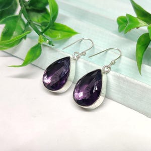 May include: A pair of silver dangle earrings with teardrop-shaped amethyst gemstones. The earrings have a simple design and are perfect for everyday wear.