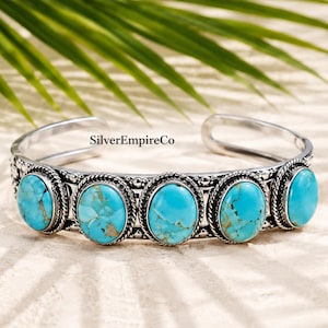 May include: A silver cuff bracelet featuring five oval-shaped turquoise stones with brown veining. The metal band has a decorative twisted rope border and small bead accents. The text SilverEmpireCo is printed on the inner surface of the band.