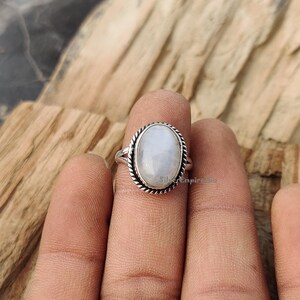 May include: A silver ring featuring an oval moonstone. The ring has a delicate, twisted band and a simple, elegant design.