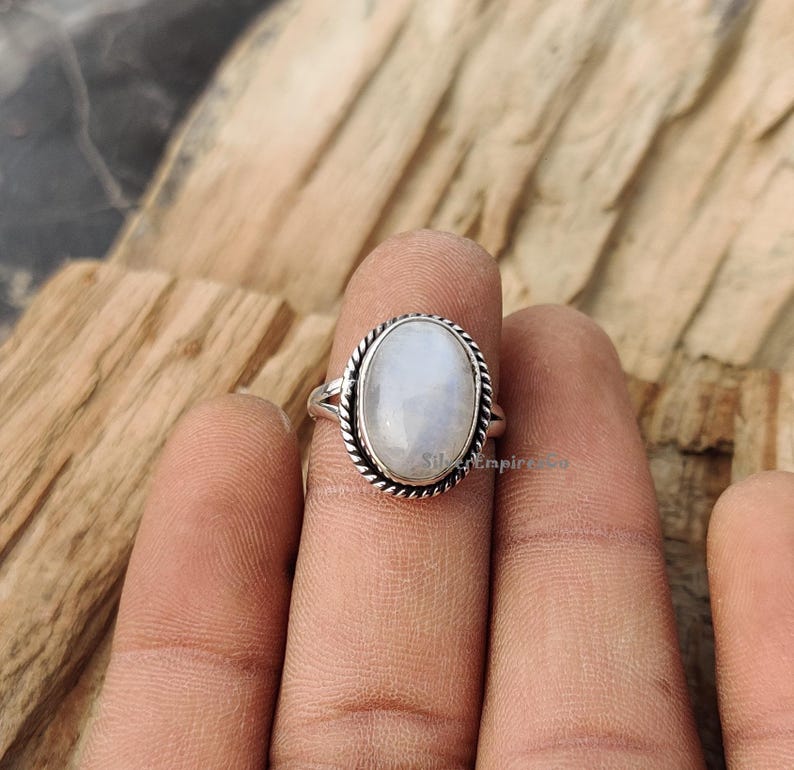 May include: A silver ring featuring an oval moonstone. The ring has a delicate, twisted band and a simple, elegant design.
