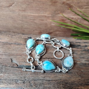 Könnte beinhalten: Ein silbernes Armband mit einem Schiebeverschluss verfügt über fünf tropfenförmige türkisfarbene Edelsteine, die in Silber gefasst sind.