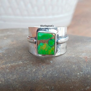 Może przedstawiać: Szeroki srebrny pierścionek z kwadratowym, zielonym turkusem osadzonym w środku. Obrączka ma fakturę młotkową i cienką srebrną linię wokół kamienia.