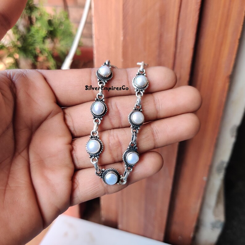 May include: A silver bracelet featuring round, white pearls set in ornate, circular frames. The bracelet is composed of multiple pearl-adorned links, connected by smaller silver links. The text "SilverEmpiresCo" is visible on the image.