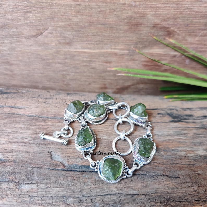 May include: A silver bracelet with green gemstone links. The bracelet has a toggle clasp and is made of sterling silver.