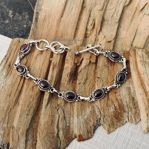 May include: A silver bracelet with a toggle clasp and oval-shaped red gemstones.