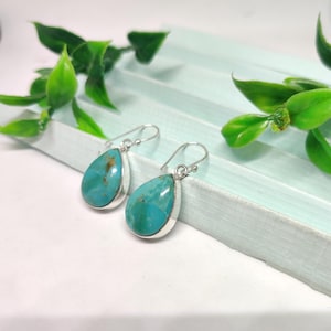 May include: A pair of silver teardrop earrings with turquoise stones. The stones are a light blue color with brown veins.