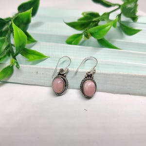 May include: A pair of silver earrings with pink oval-shaped stones. The earrings have a delicate design with a small silver loop at the top.