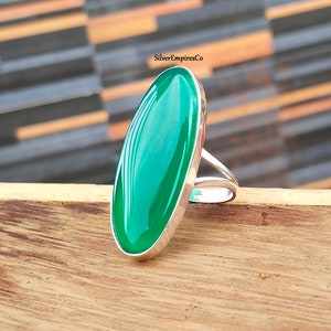 May include: A silver ring with a large oval green gemstone. The ring is set on a wooden surface.